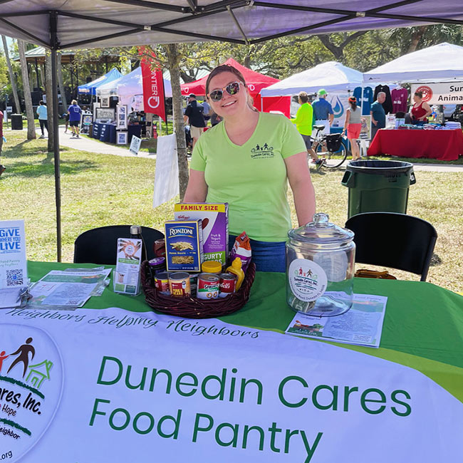 Dunedin Cares Food Pantry tent with a volunteer under it