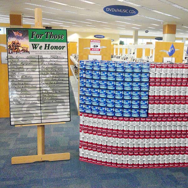 Canned goods arranged in the shape of the American flag with a sign next to it stating "For Those We Honor"